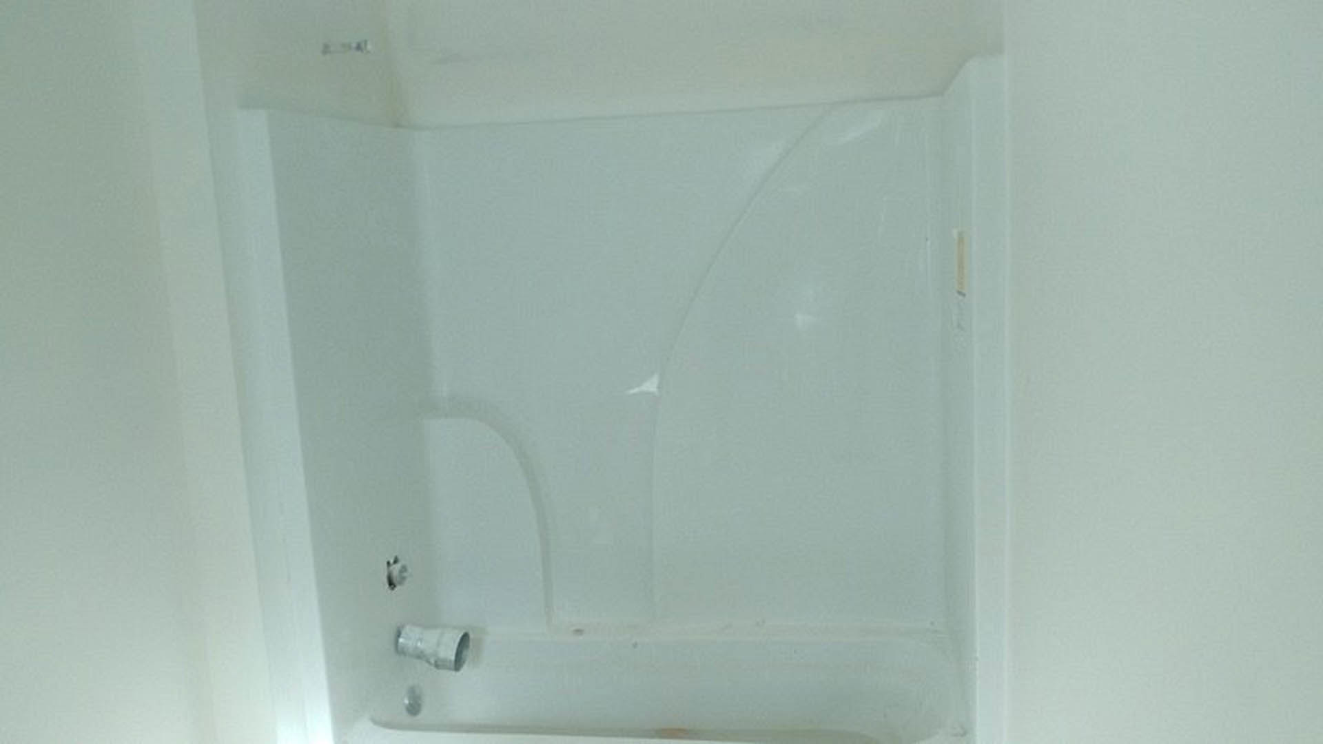 Freestanding white bathtub with chrome faucet against light-colored tiled bathroom wall