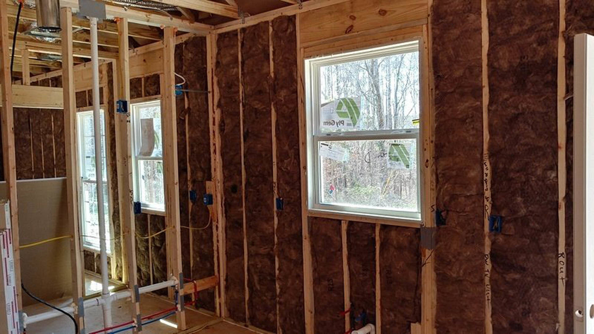 Unfinished room with exposed wood framing, multiple windows, yellow hose, electrical cable, and metal beam.