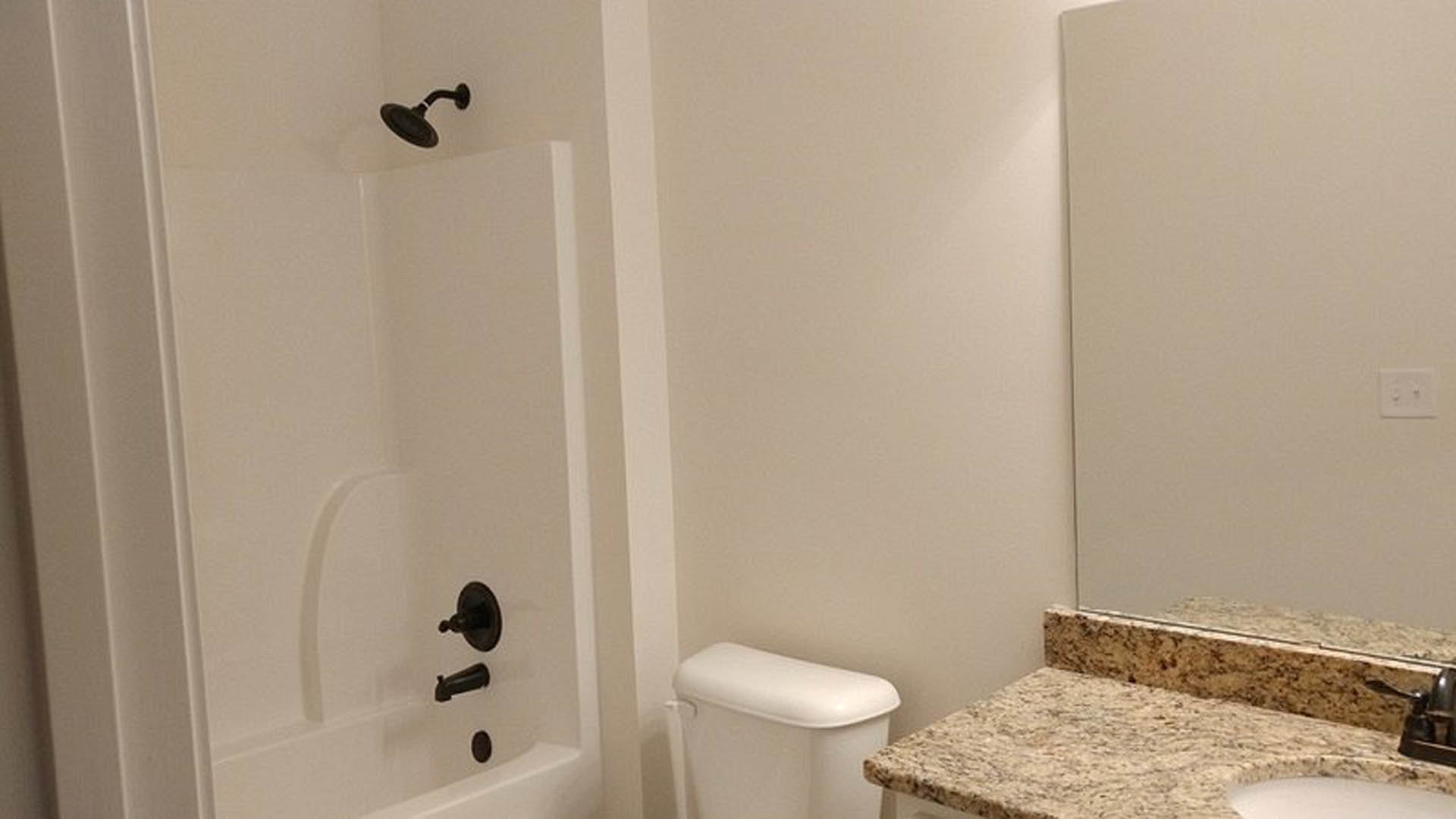 Marble countertop with undermount sink, chrome faucet, white tile backsplash, and adjacent white toilet tank