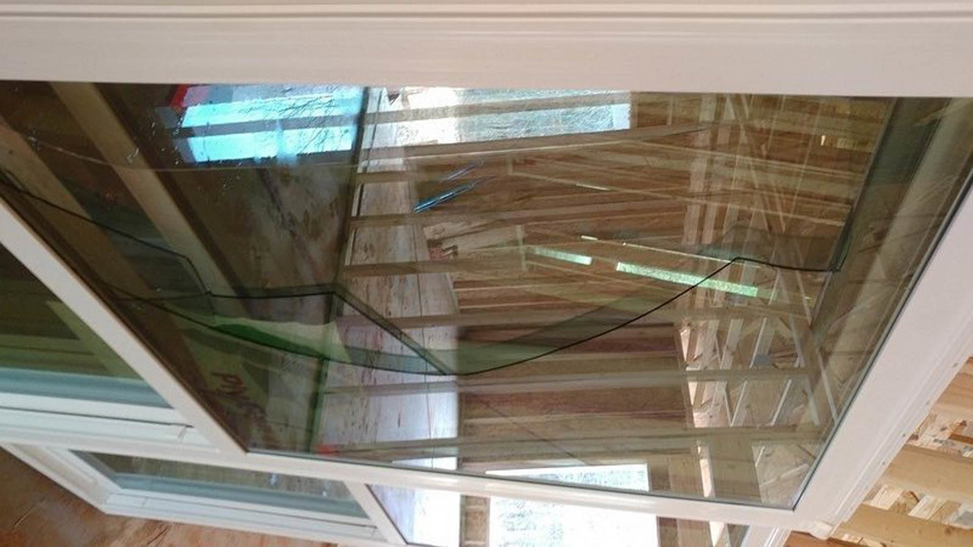 Glass door with shattered glass panel, adjacent to blue and white striped wall, wood flooring, and glass table with white frame in indoor residential space.