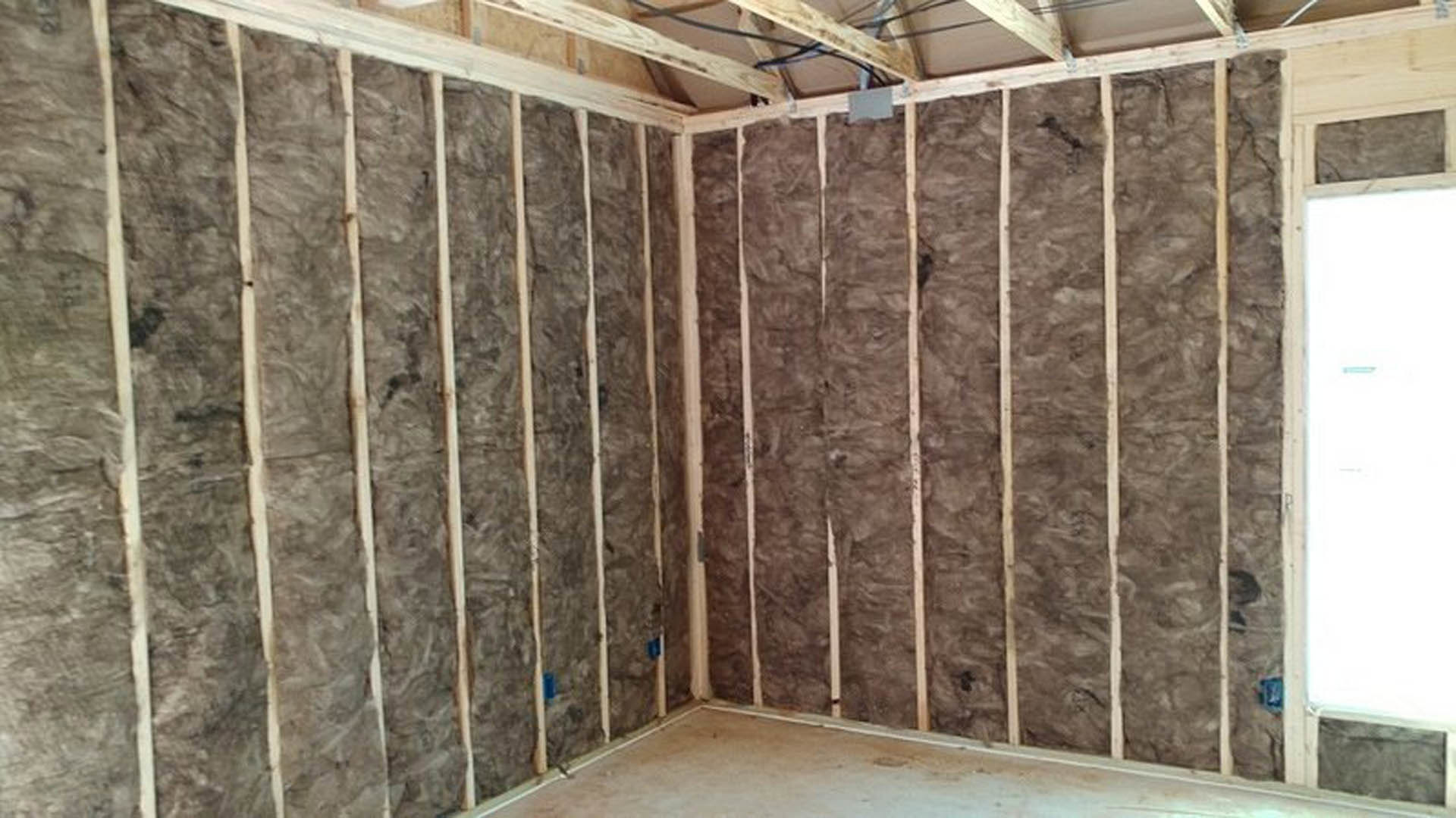 Wood-paneled room with exposed ceiling beams, white door, and visible wall insulation
