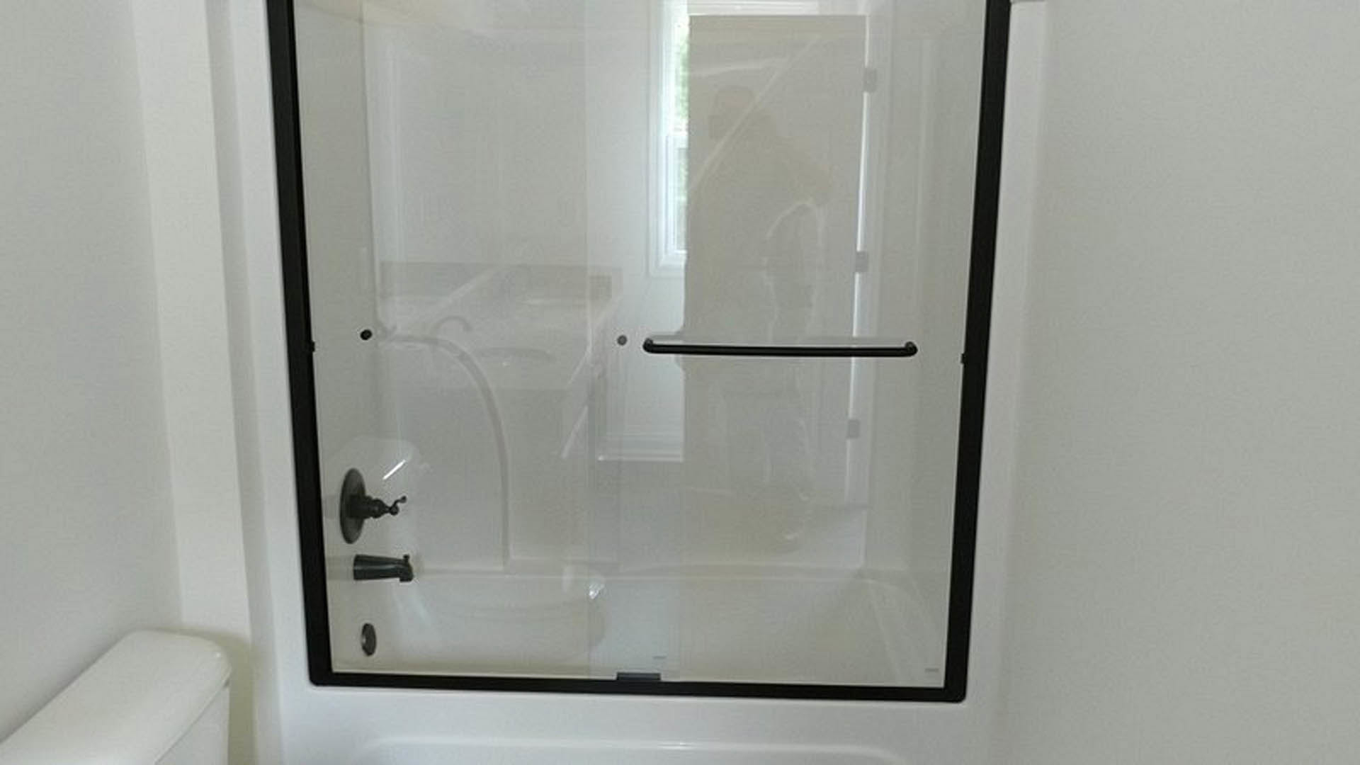 Frameless glass shower door with chrome hardware beside white tiled walls in modern bathroom