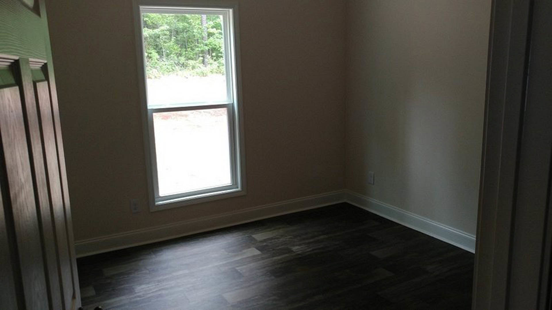 Dark wood flooring and wooden chair in a bright room with large window overlooking trees.