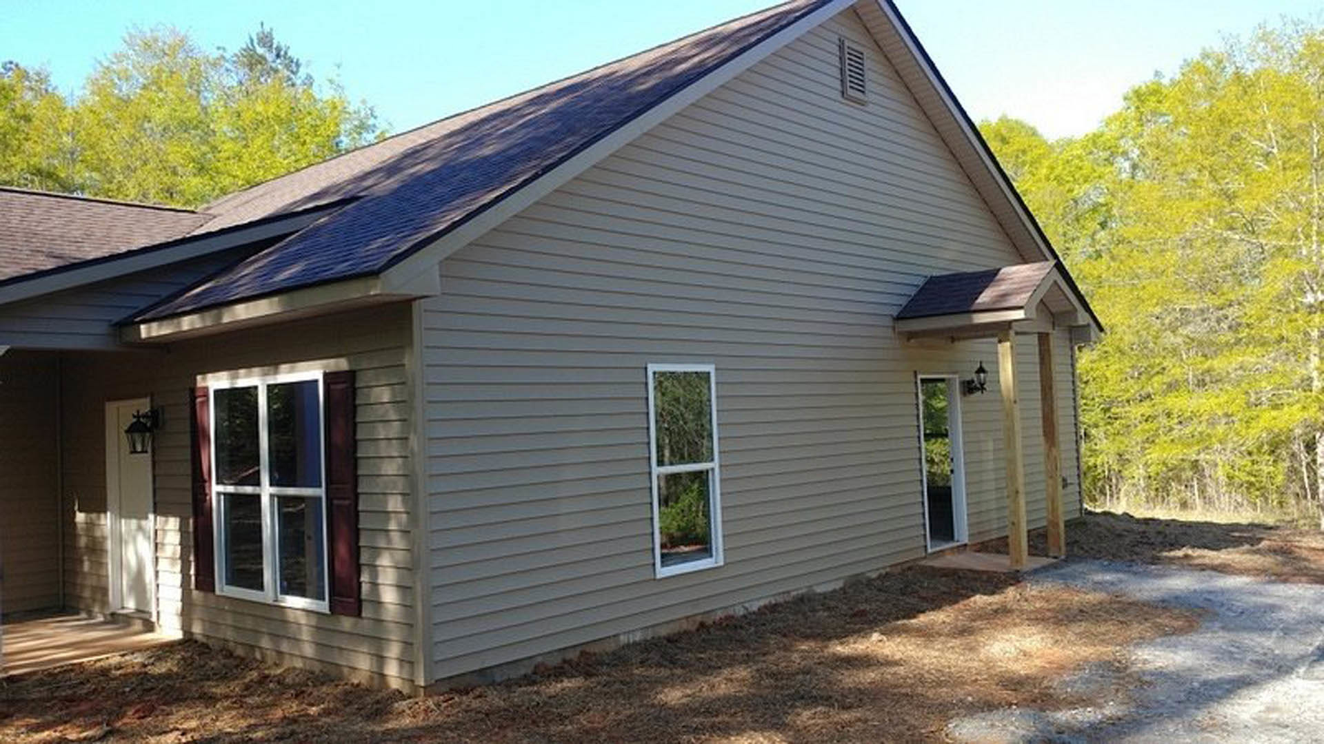 Two-story house with white siding, covered front porch, white-framed windows, dark shingle roof, and outdoor lantern, surrounded by green trees.