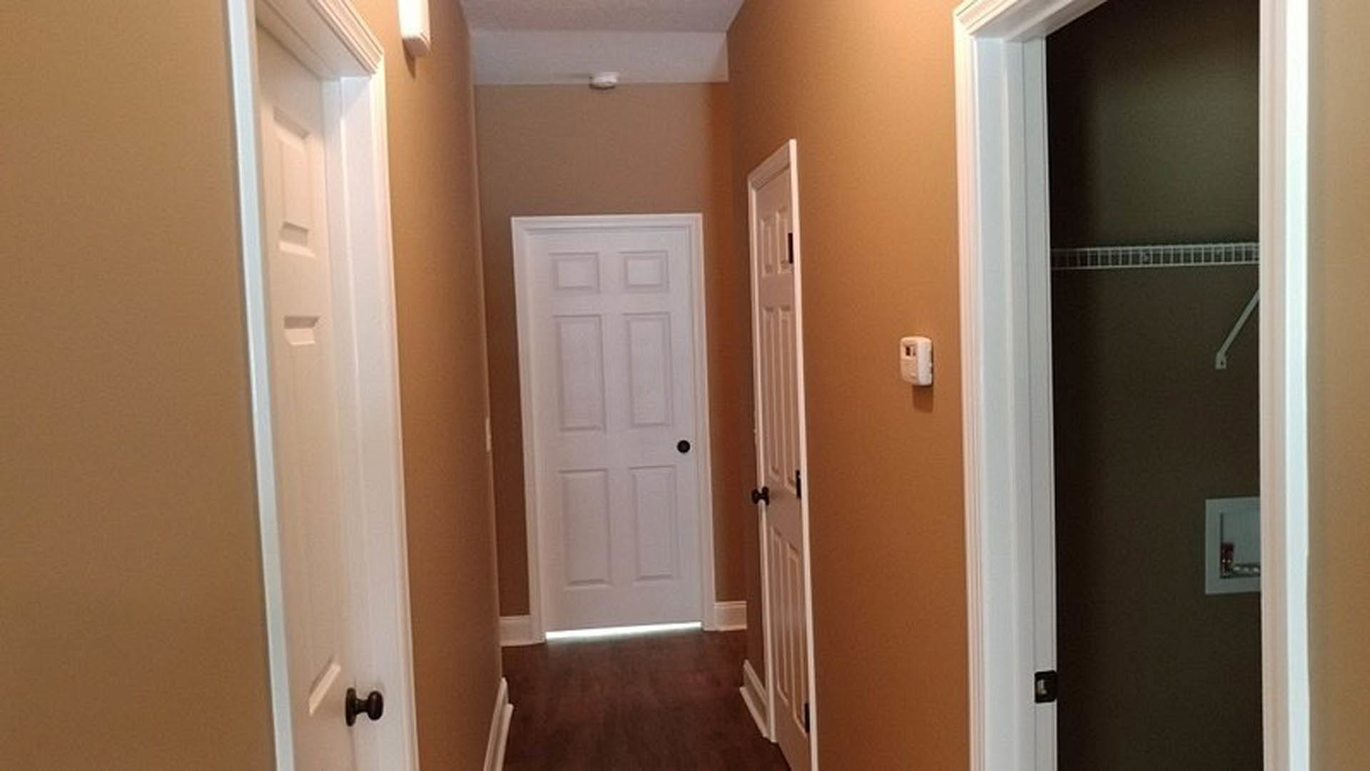 Hallway with white paneled doors, black handles, light plaster walls, and smooth flooring