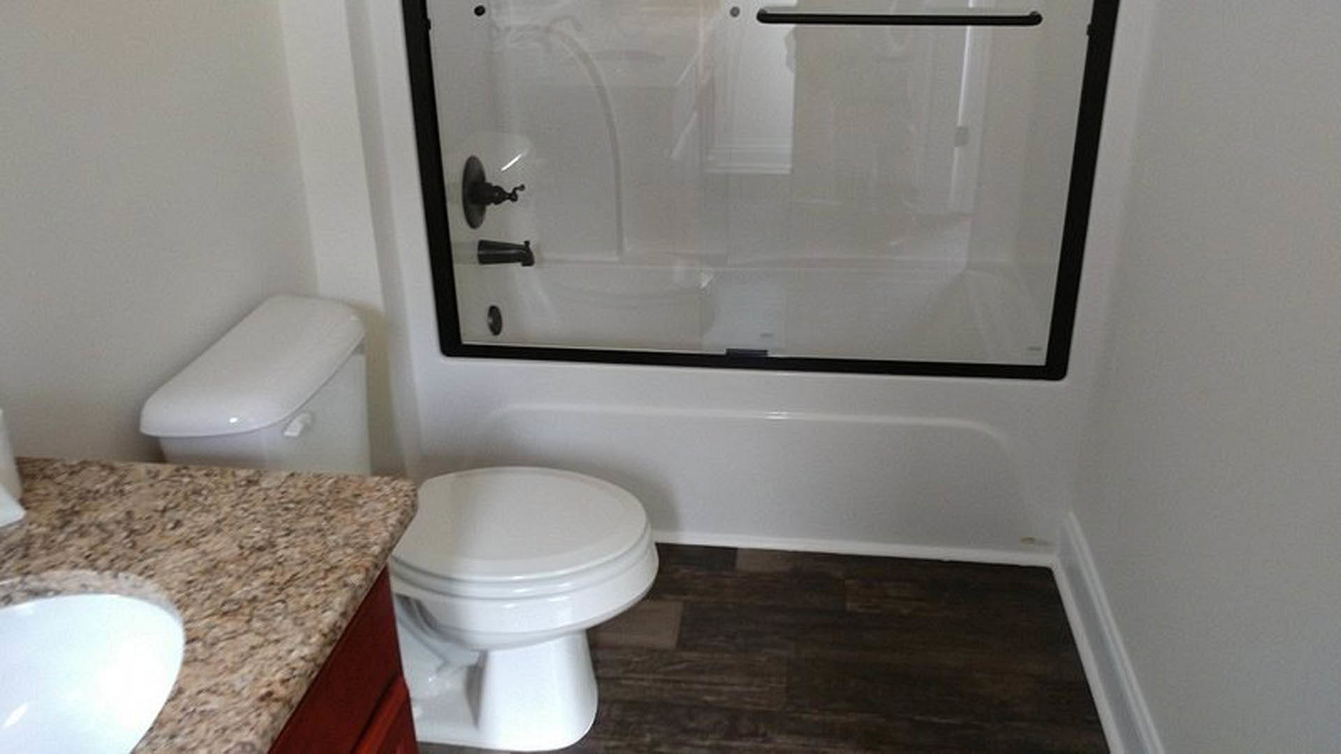 Bathroom with glass shower enclosure, white toilet and sink, light tile flooring, wall-mounted mirror, and chrome fixtures