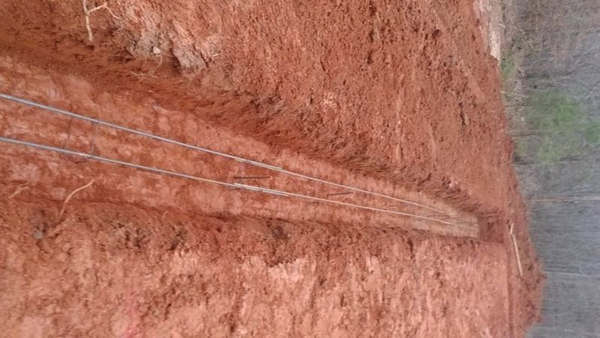 Dirt field with upright metal poles spaced across bare ground, surrounded by sparse grass and open outdoor landscape