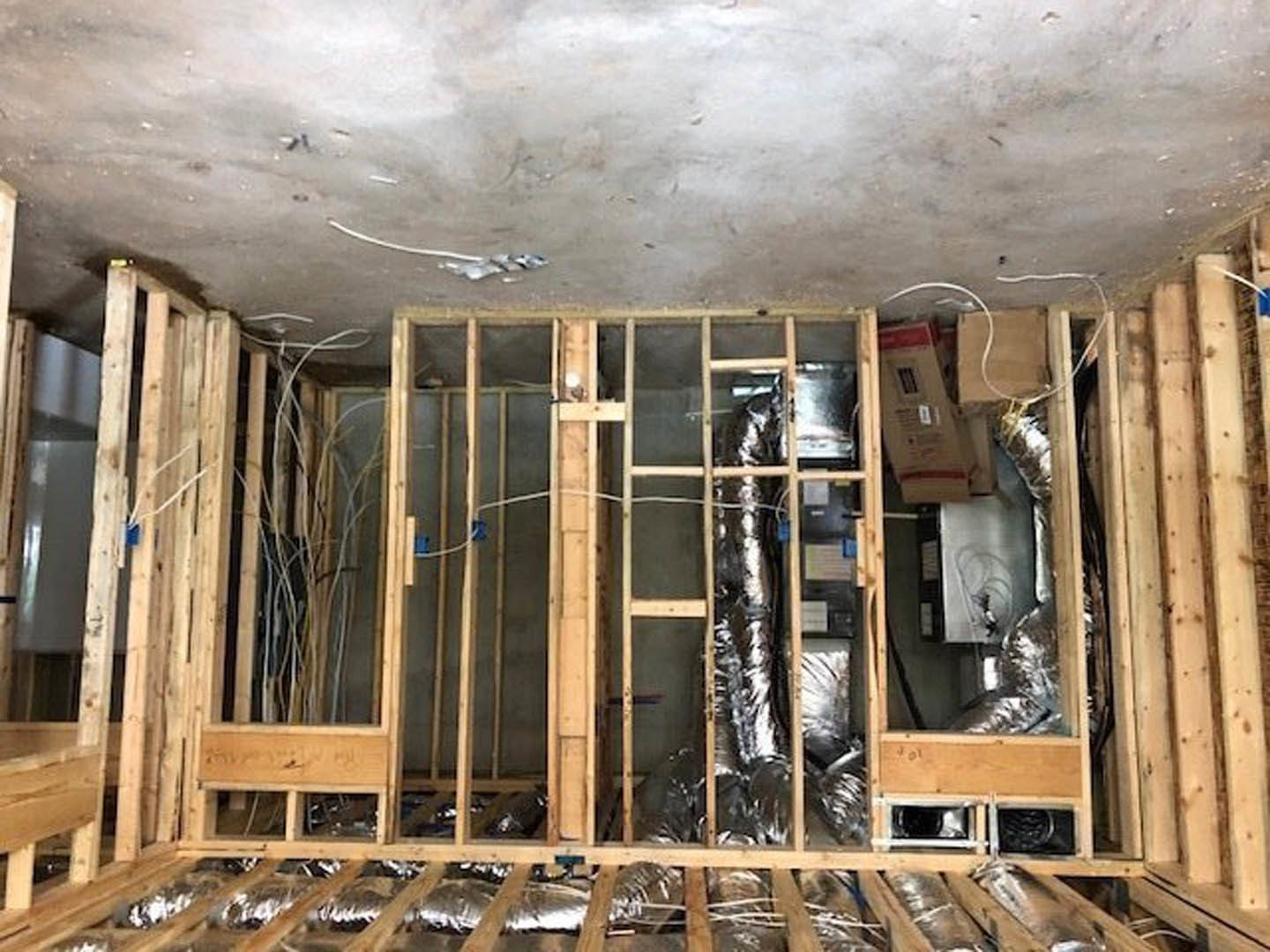 Unfinished room with exposed beams, silver foil insulation on walls and ceiling, visible electrical wires, and construction materials scattered on the floor