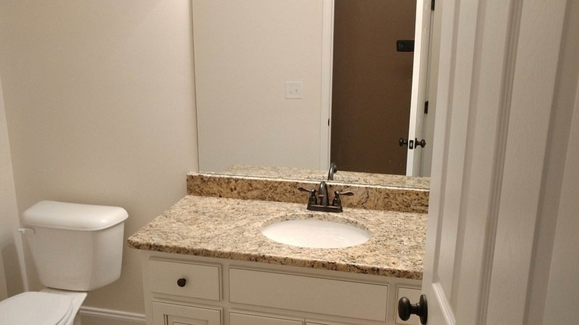 Marble countertop with undermount sink, chrome faucet, white toilet, light switch on white wall, tile flooring