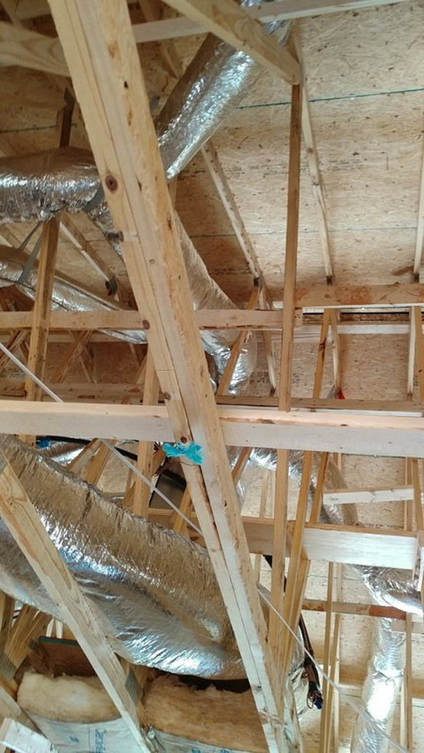 Exposed wood beams and metal pipes in unfinished building interior with metal foil roof insulation