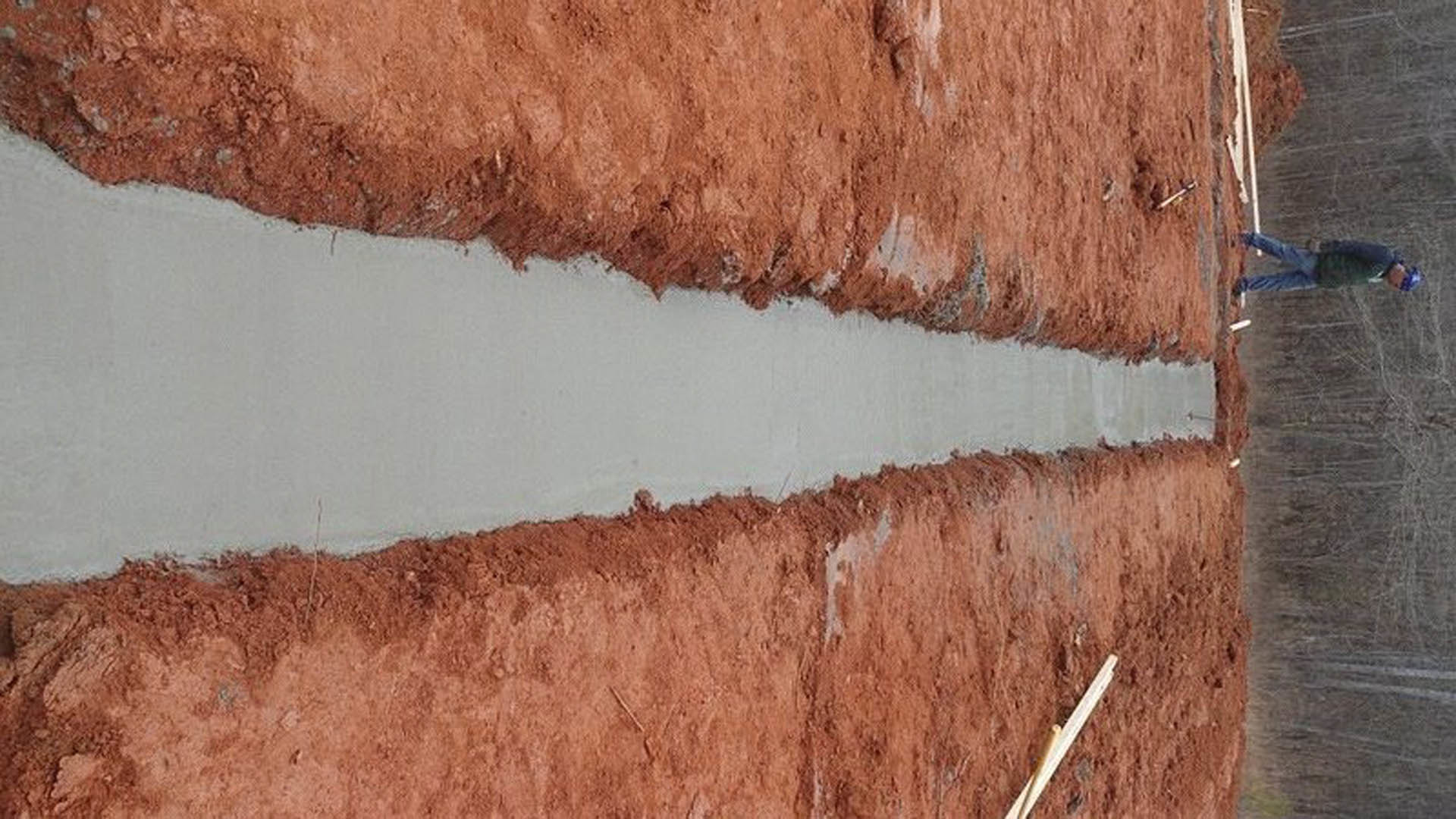 Freshly poured gray concrete foundation forming a long strip through brown dirt on an outdoor residential construction site
