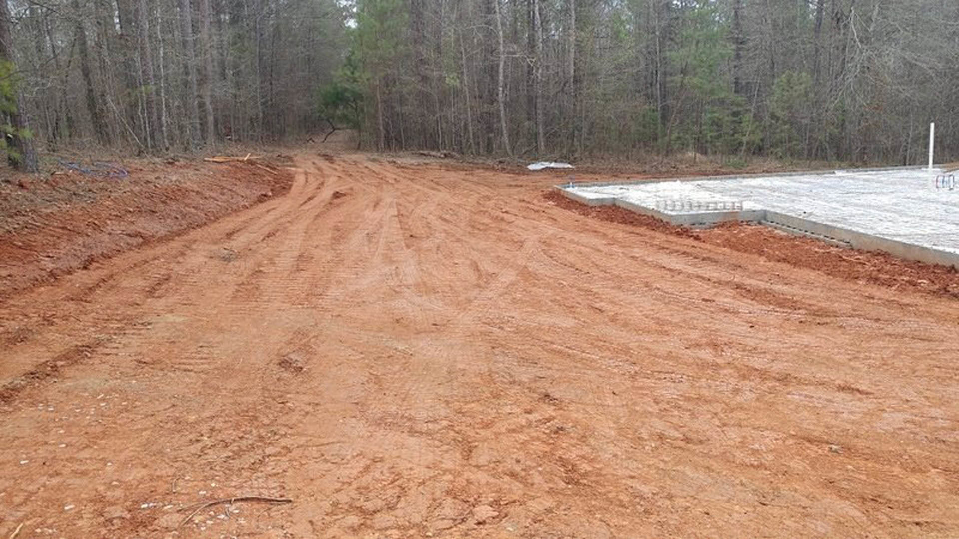 Concrete foundation set beside a dirt road, surrounded by tall trees and forested landscape