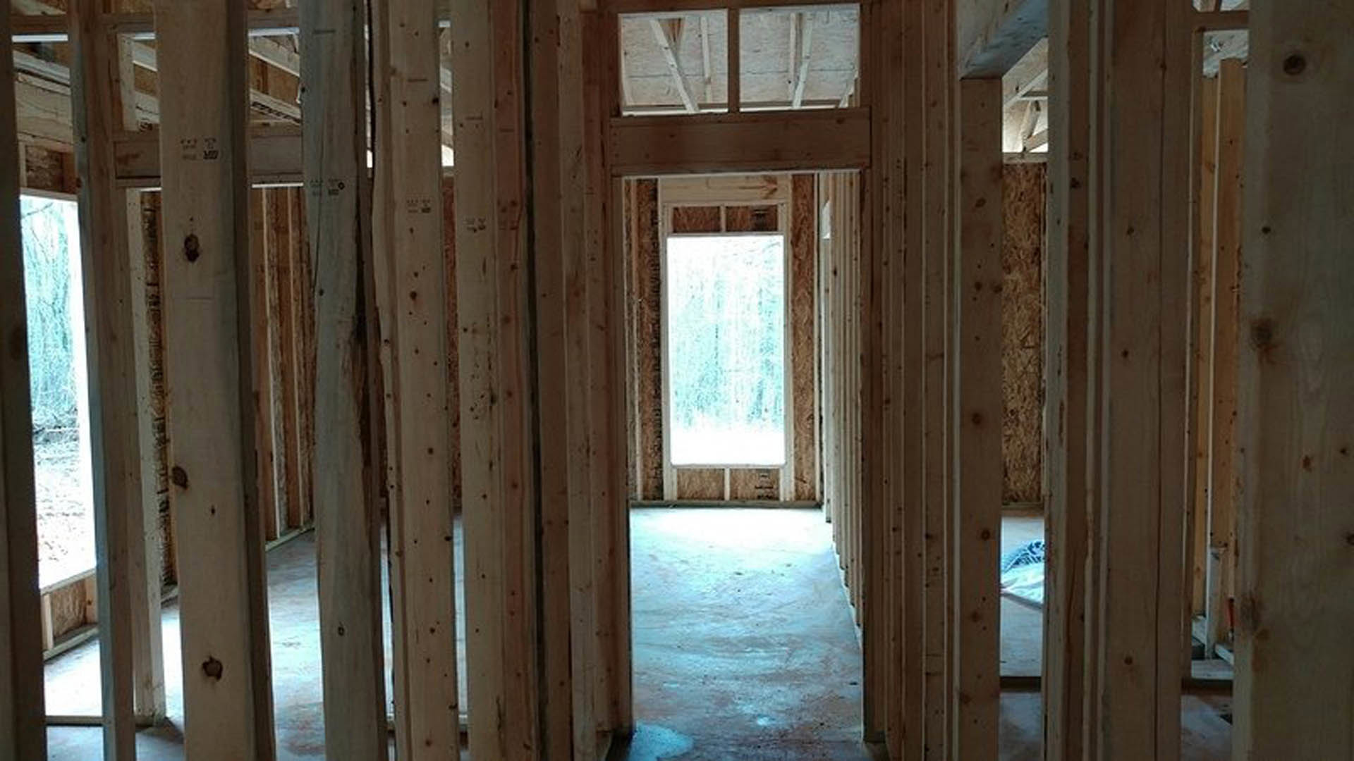 Living room with exposed wood ceiling beams, large window with frosted glass, and natural light streaming through doorway onto hardwood floors