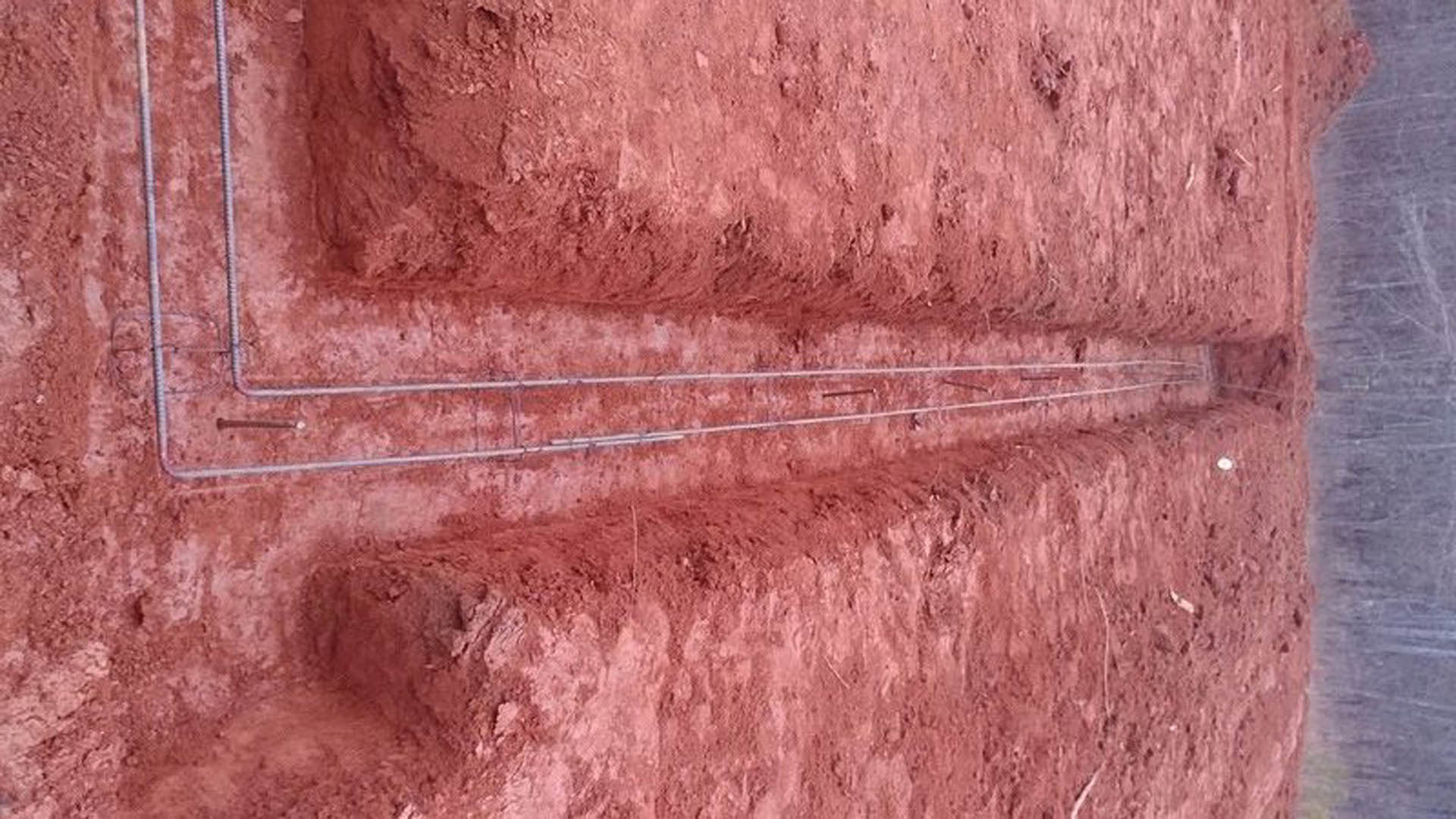 Exposed wire partially buried in red-brown dirt with rough soil texture