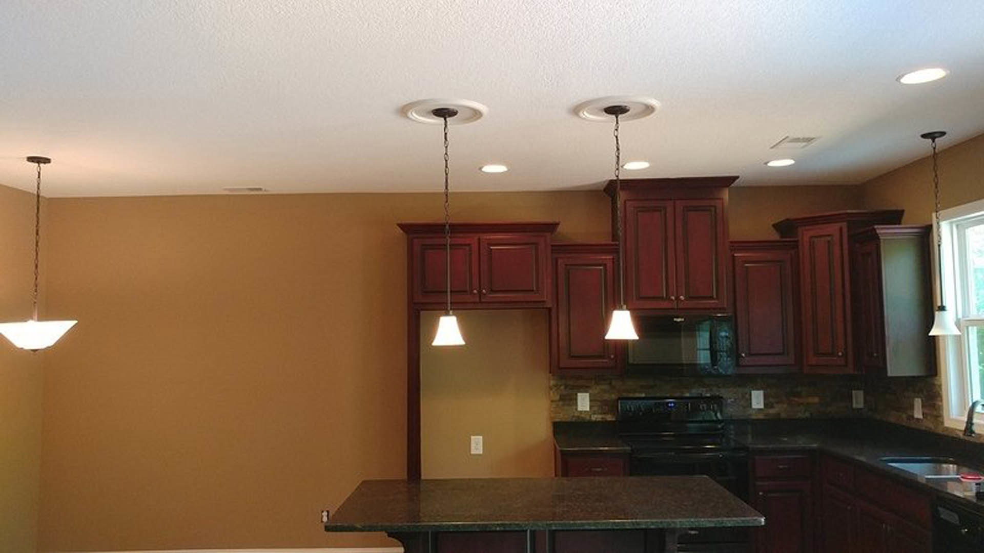 Modern kitchen featuring a central island with stone countertop, pendant lights above, white cabinetry, stainless steel sink, and built-in appliances against neutral walls.