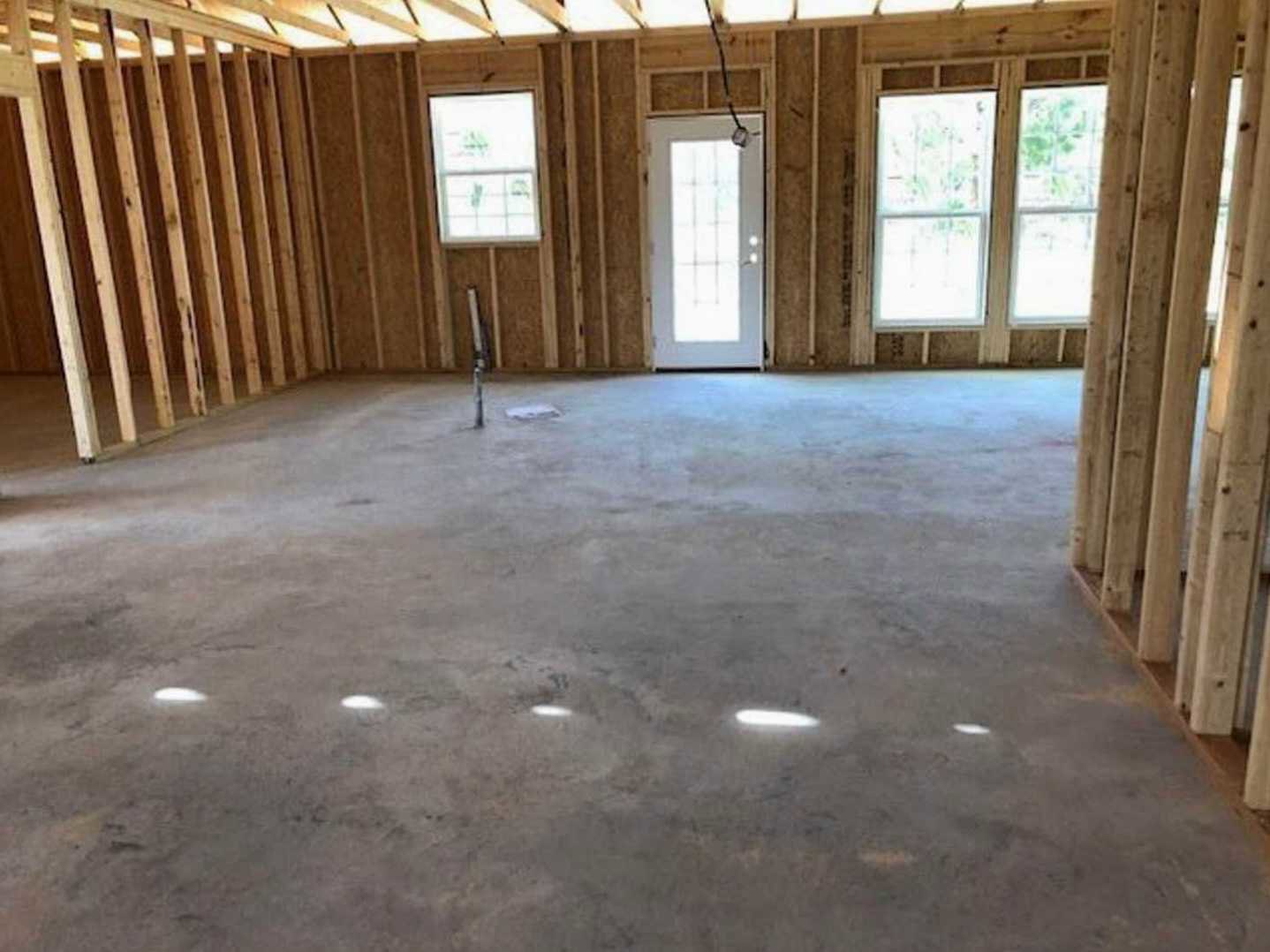 Concrete floor room with recessed ceiling lights, white door featuring glass window, large window framed in white with sheer curtain and green leaf pattern