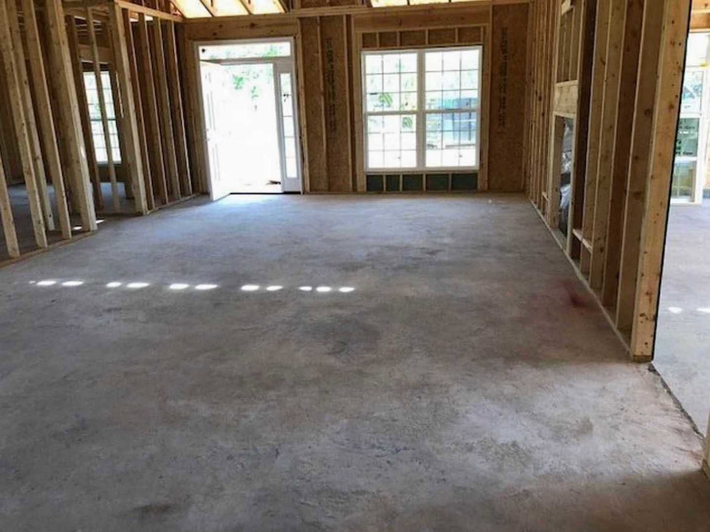 Concrete floor with sunlight streaming through multi-pane window, white door with glass panes, exposed wood beams, white square wall feature, and ground light fixture.