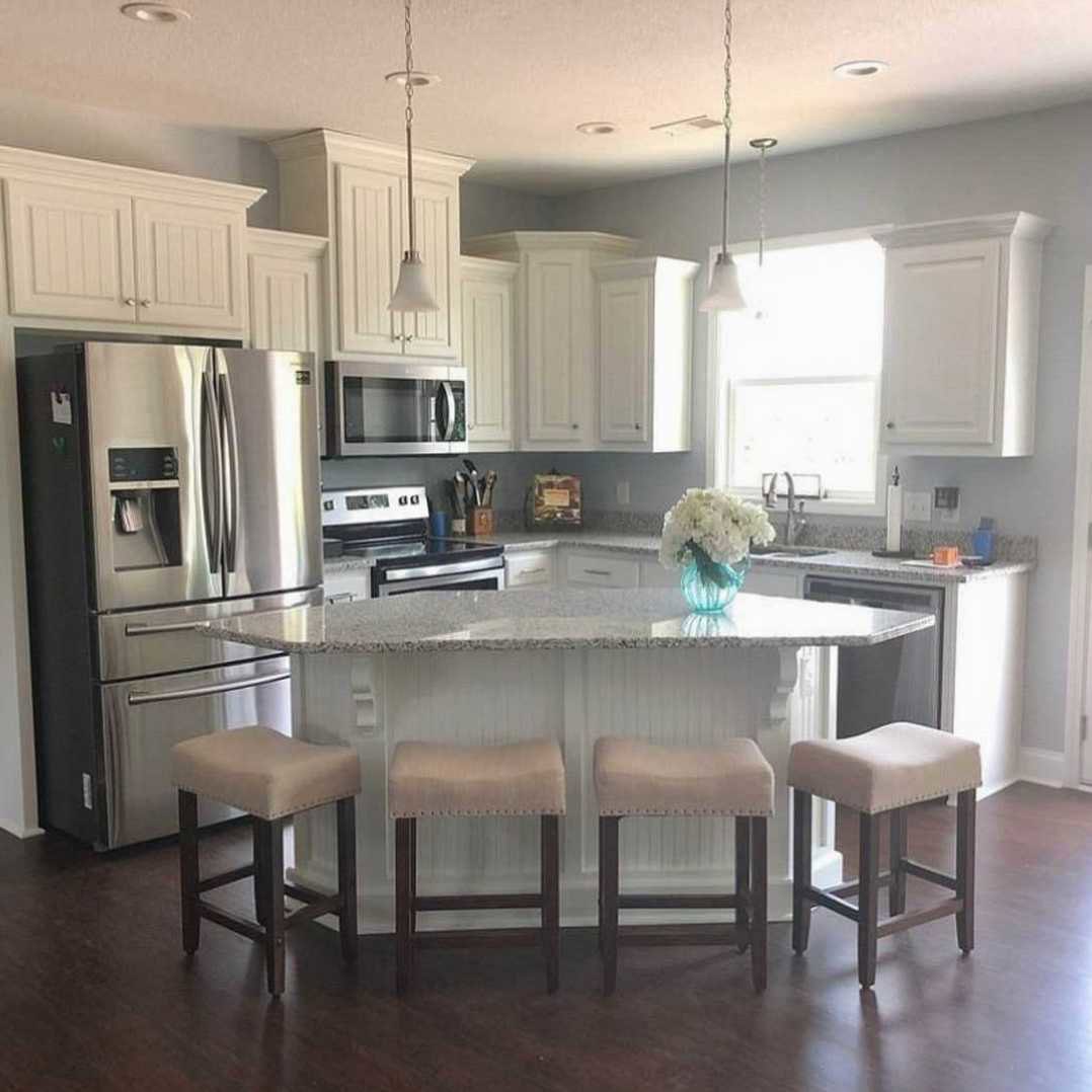 Modern kitchen featuring a marble-topped bar with cushioned stools, stainless steel refrigerator, built-in microwave, white cabinetry, and a vase of white flowers on the counter.
