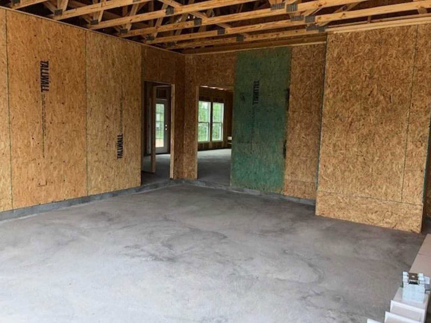 Concrete floor room with exposed wooden beams, white walls, single door, and window overlooking greenery