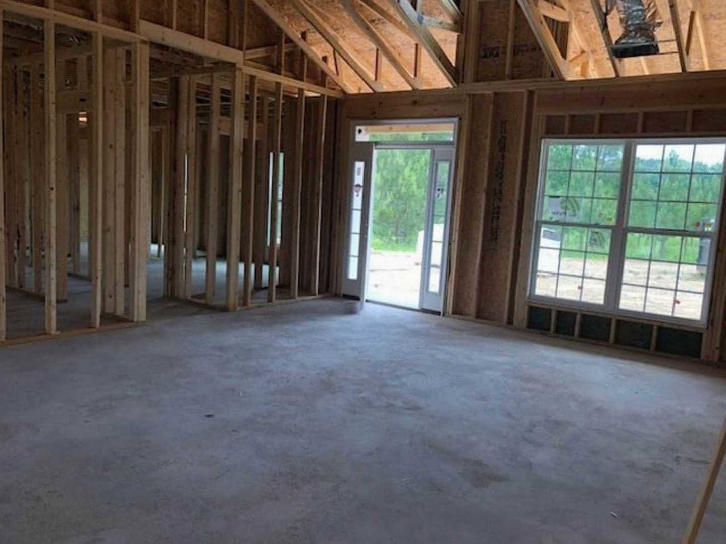 Sunlit room featuring a wooden floor, exposed ceiling beams, multi-pane windows, and a glass-paneled door opening to a view of a green tree.