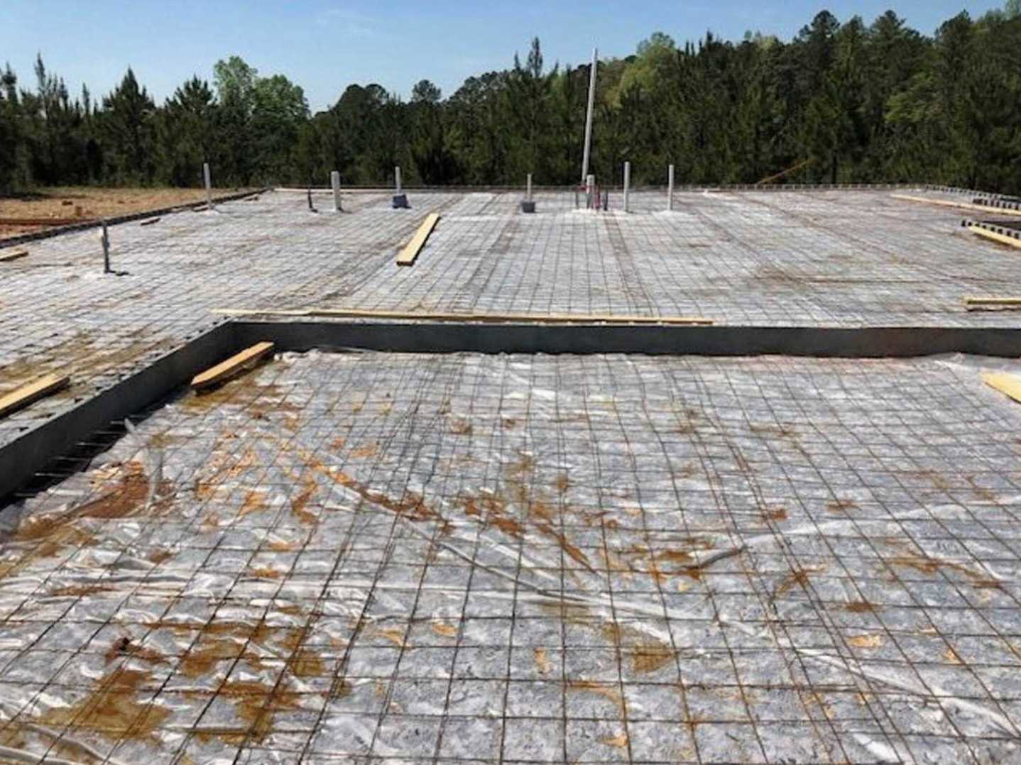 Framed custom home under construction with exposed metal grid, tall pole, and surrounding trees in background