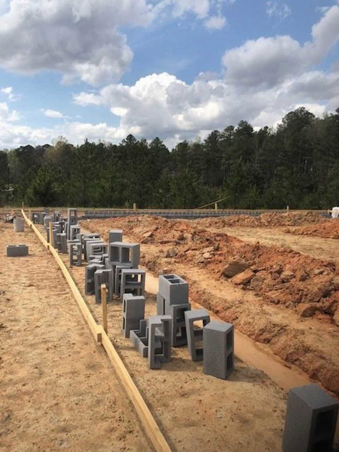 Concrete blocks stacked on dirt ground at construction site, trees and blue sky with clouds in background