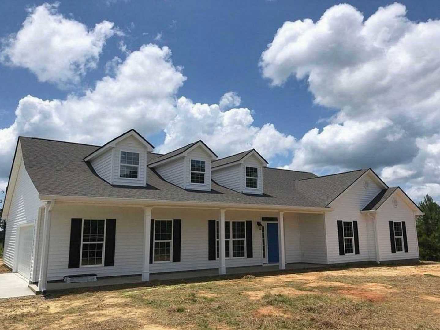 White siding home with multiple windows, blue front door, grassy lawn, and clear blue sky