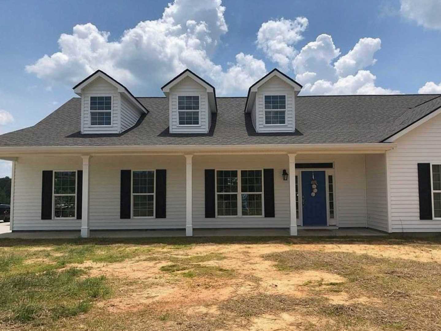 Two-story house with white siding, blue front door with white trim, dormer windows on roof, covered porch, and cloudy sky in background