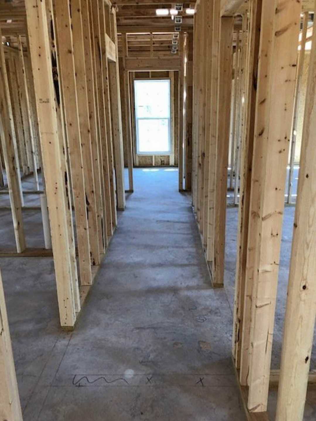 Hallway with exposed wooden ceiling beams, concrete floor, large window letting in natural light, close-up details of wood beam and door, black accent line on grey surface
