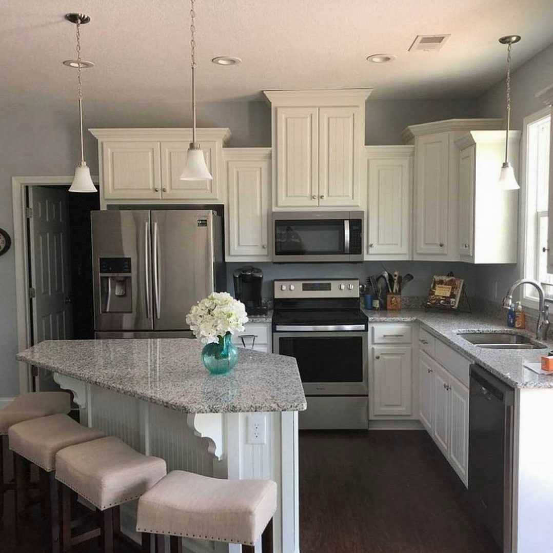 Marble kitchen island with upholstered stools, stainless refrigerator, built-in microwave, white cabinetry, vase of white flowers on countertop
