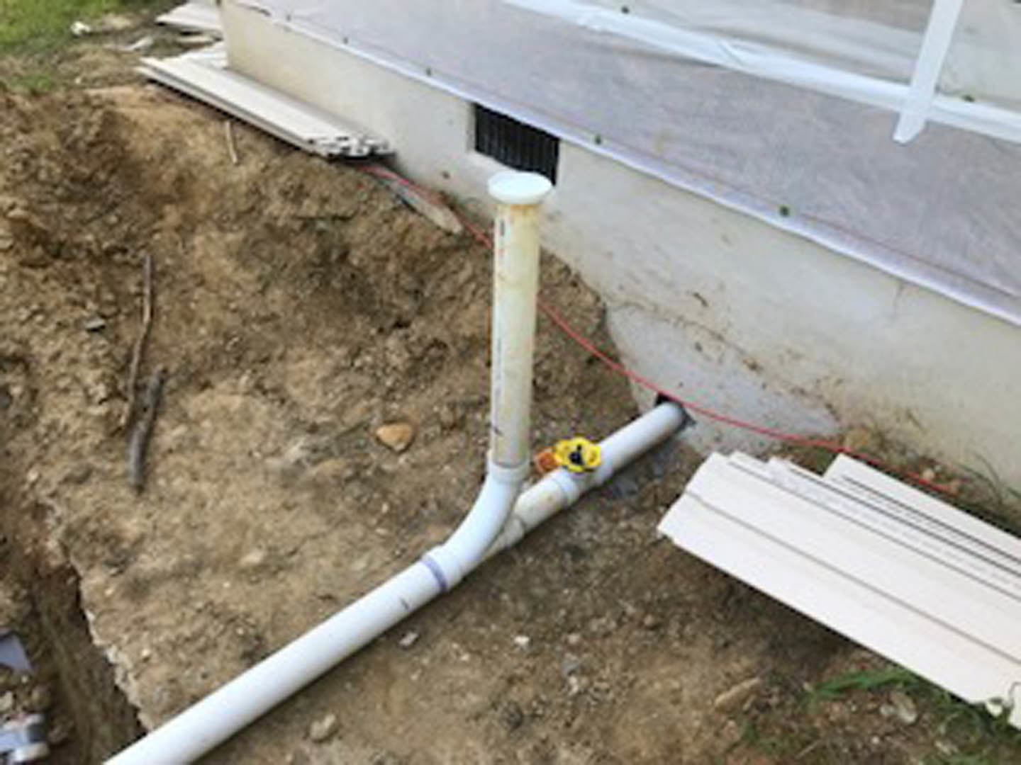 White plastic pipe lying on bare dirt outdoors near grass, part of home foundation construction.
