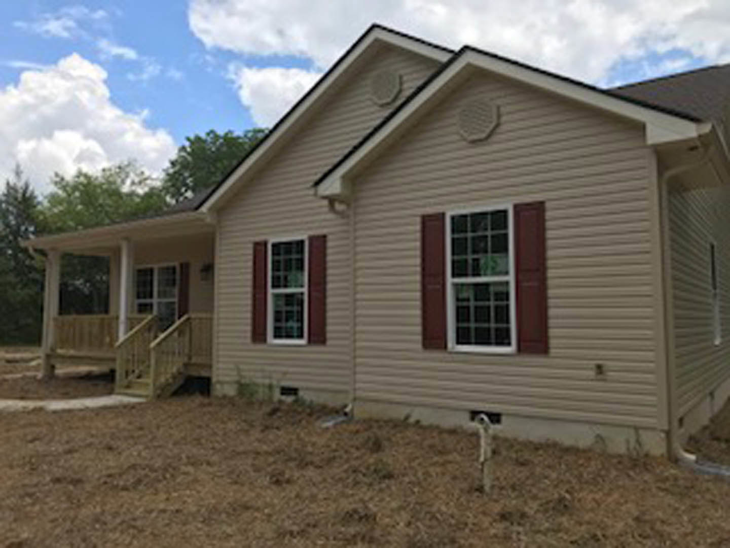 Two-story home with light siding, covered front porch, white-framed windows with shutters, and a staircase leading to the entrance under a cloudy sky.