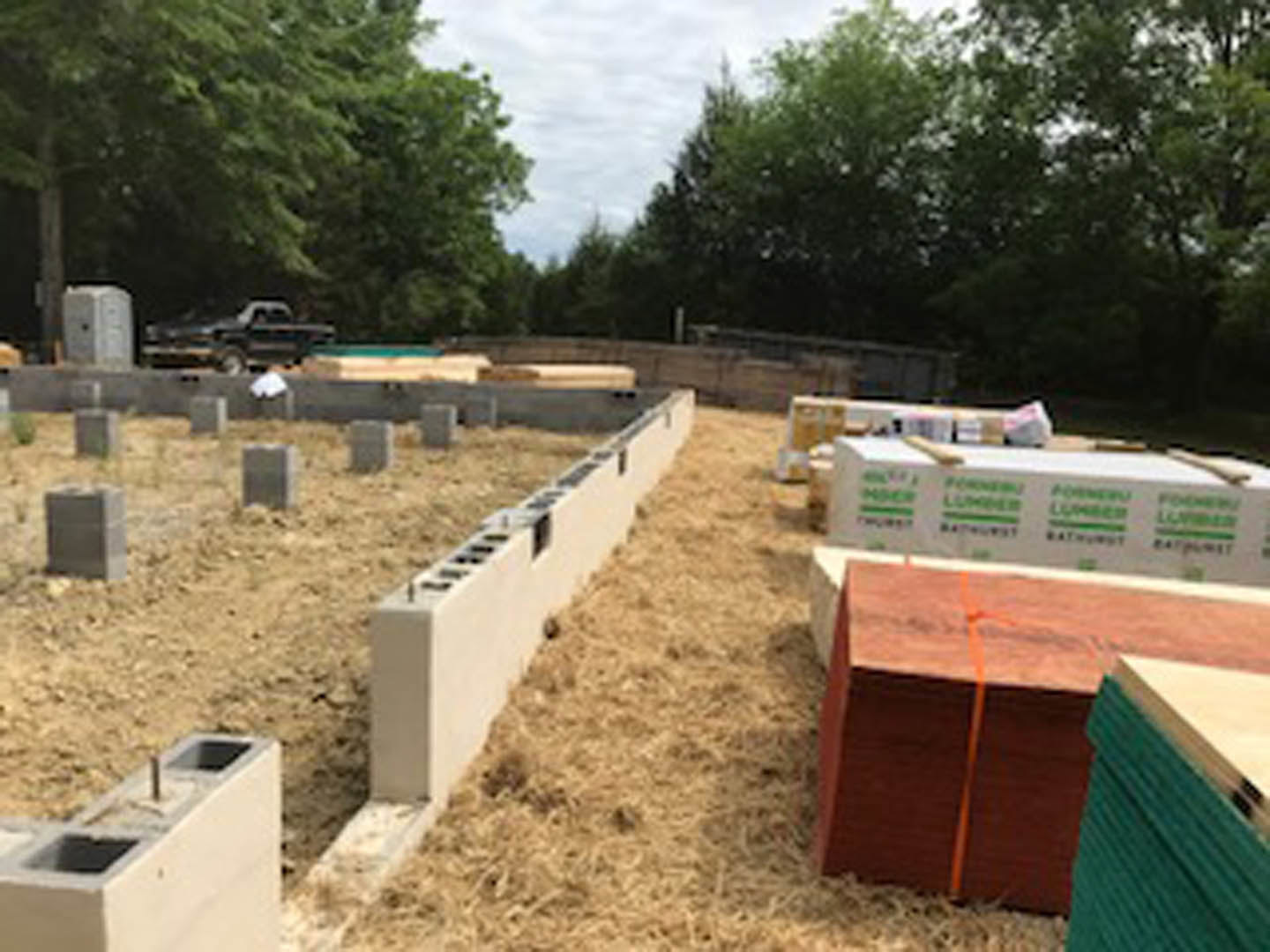 Construction site with stacked concrete blocks and bricks on bare ground, surrounded by trees and open sky