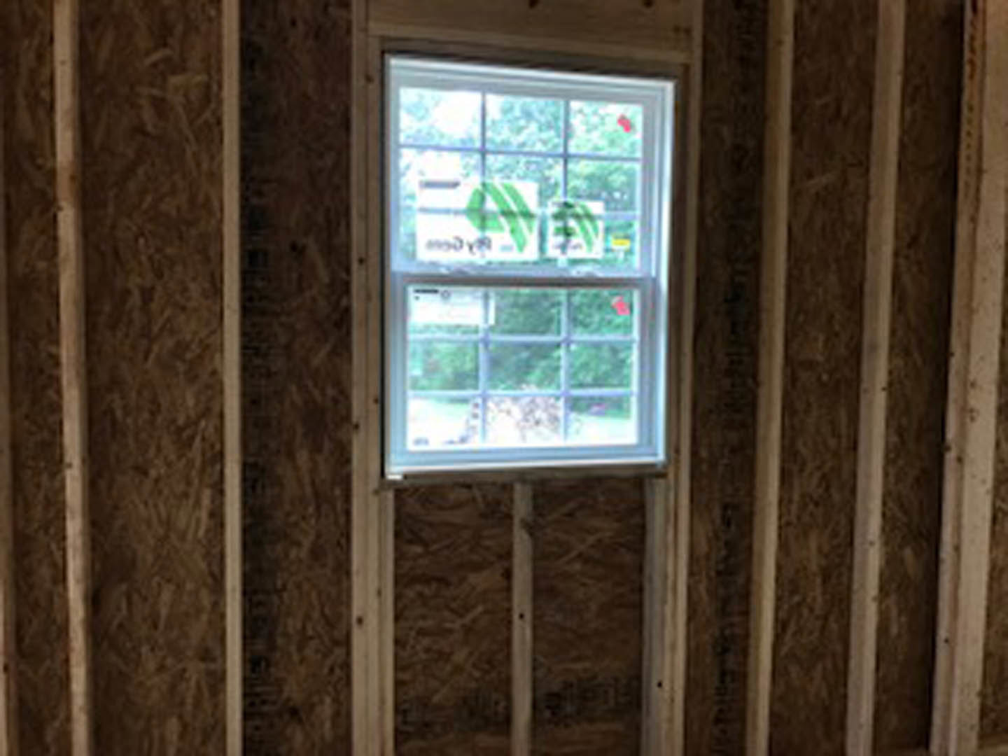Large wood-framed window set in a neutral-toned wall, natural light illuminating the remodeled interior room with visible wooden trim and subtle signage on the glass.
