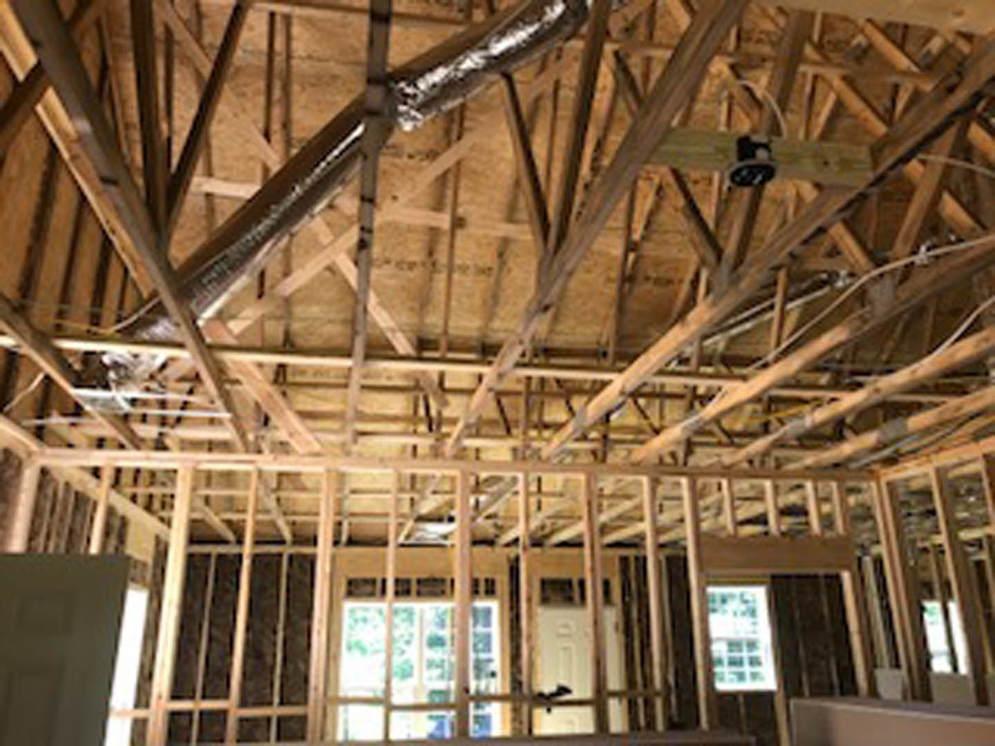 Exposed wood framing with steel beam and metal pipe on ceiling, partially visible window and door, construction materials indoors