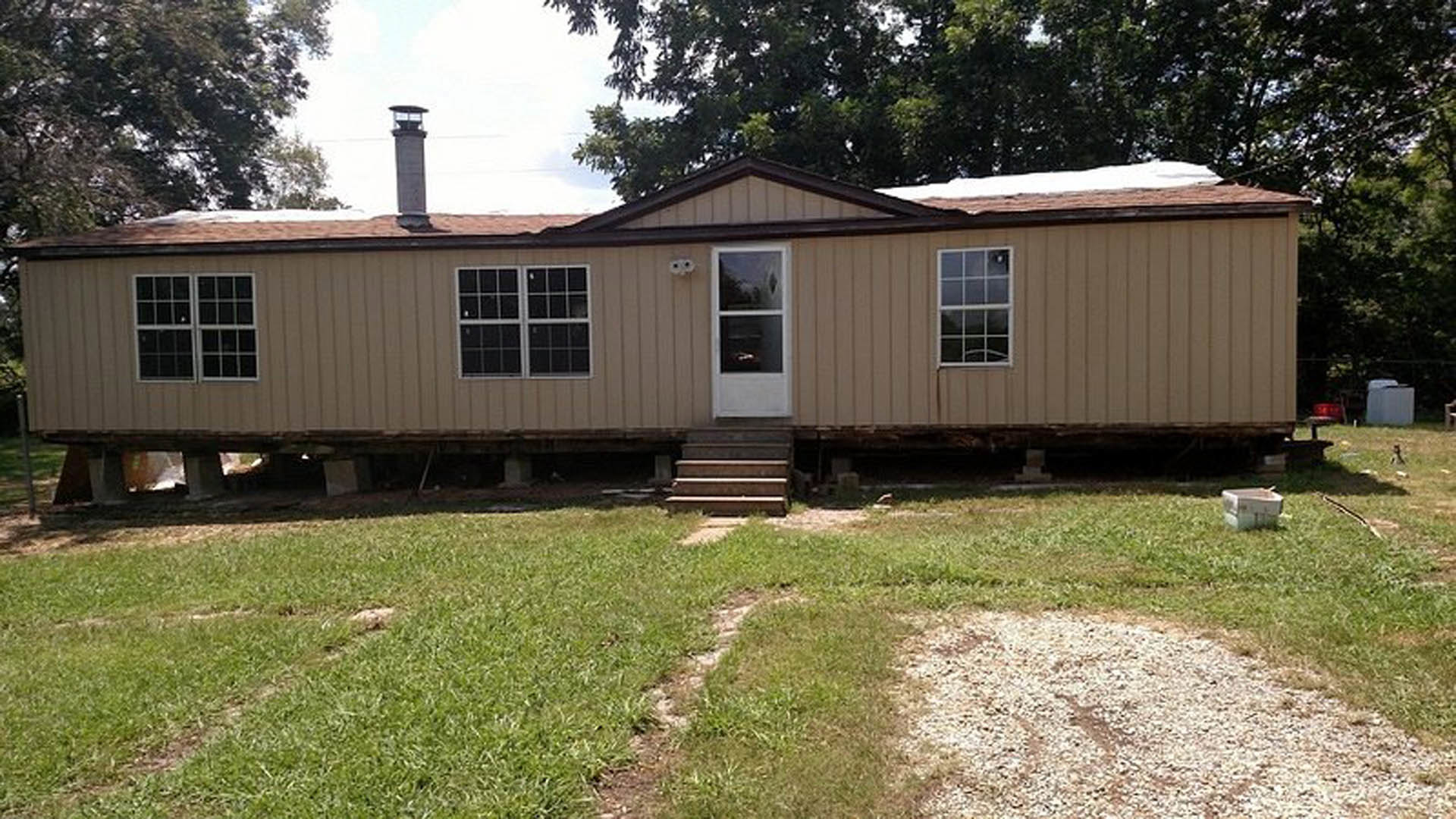 Two-story custom home with white framed windows, glass pane door, front steps, manicured green lawn, and mature trees in the yard