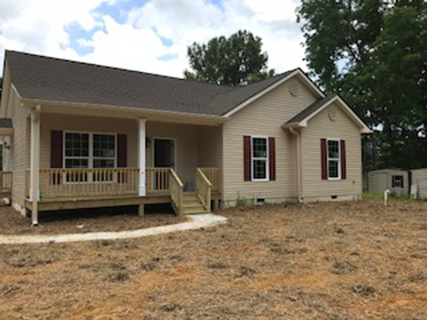 Two-story house with light siding, covered front porch featuring white railing and stairs, grassy yard with mature trees, large windows with white frames, blue sky in background