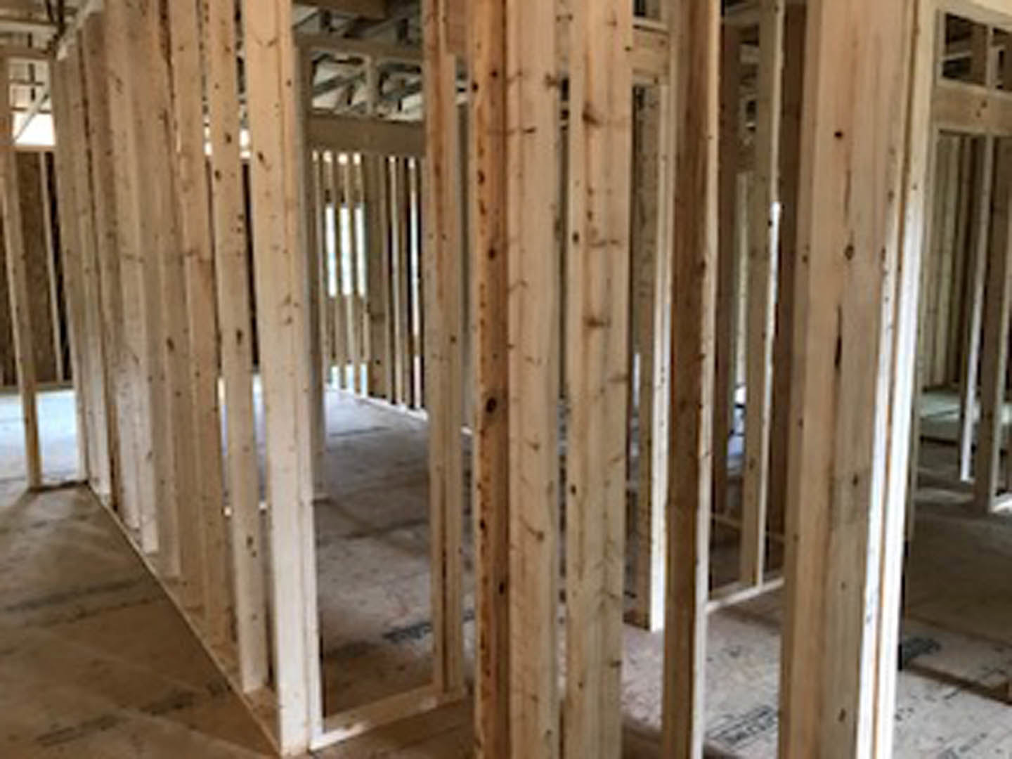 Exposed wood framing and beams inside a residential home under construction, with visible lumber and insulation materials