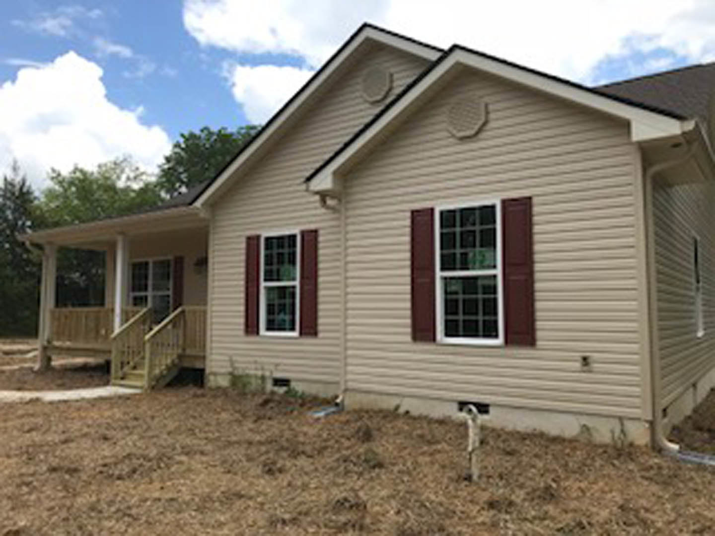 Two-story home with light siding, covered front porch, white-framed windows, and gabled roof under partly cloudy sky