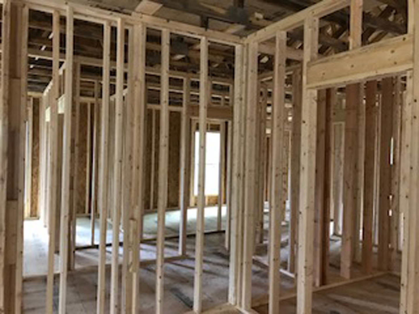 Room under construction with exposed wood framing, ceiling beams, unfinished floor, and a window letting in natural light
