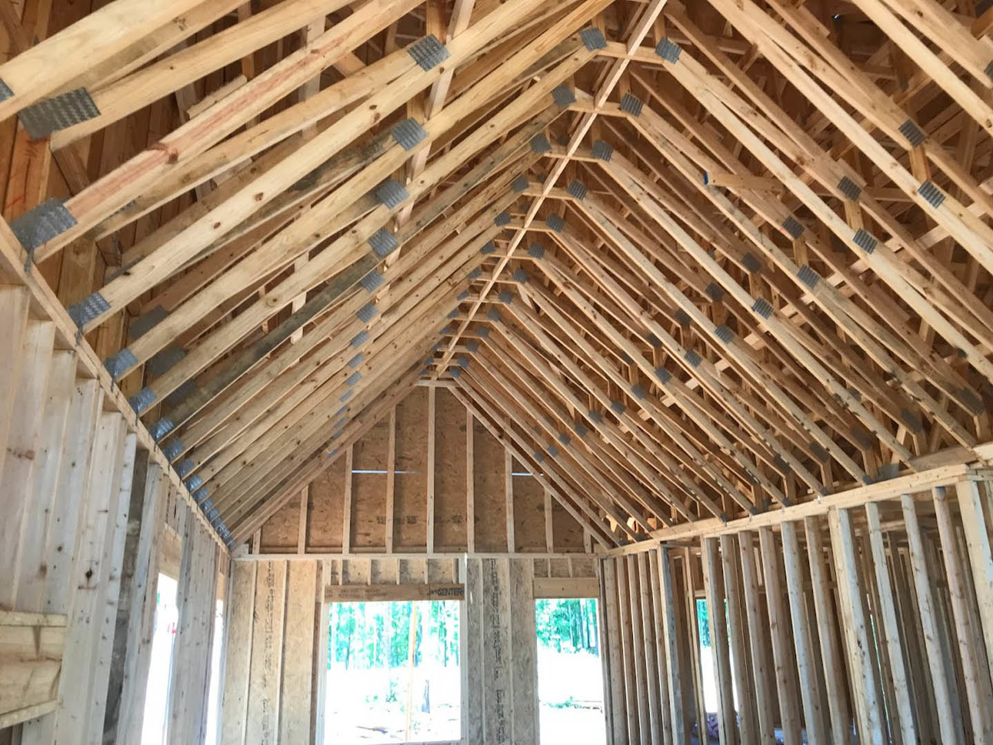 Exposed wood framing and beams inside a house under construction, with unfinished walls and a window displaying a sign.