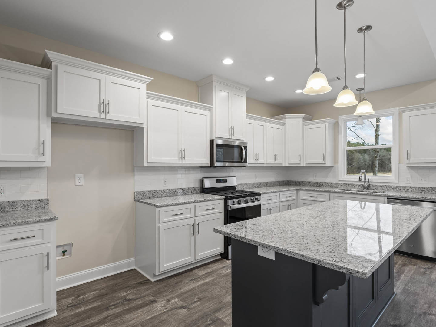 White kitchen with granite countertops, marble island, stainless steel microwave, stove and oven, white cabinets with silver handles, and undermount sink.