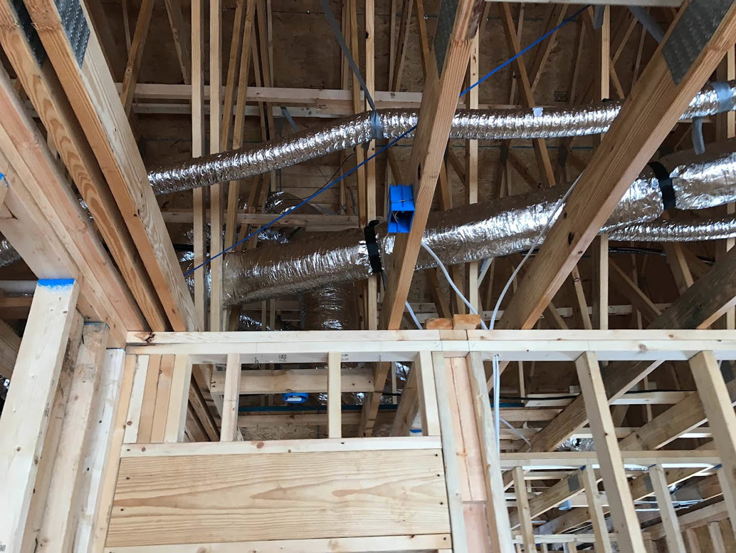 Exposed metal pipes running through unfinished wooden ceiling framing, blue electrical box with wires, construction materials and insulation visible