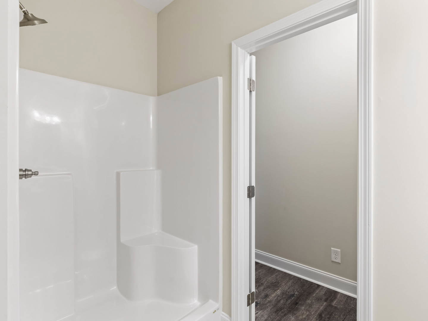 Bathroom with freestanding white tub, white paneled door, white tile walls, built-in shower seat, wood flooring with white baseboard, chrome fixtures, and modern lighting.