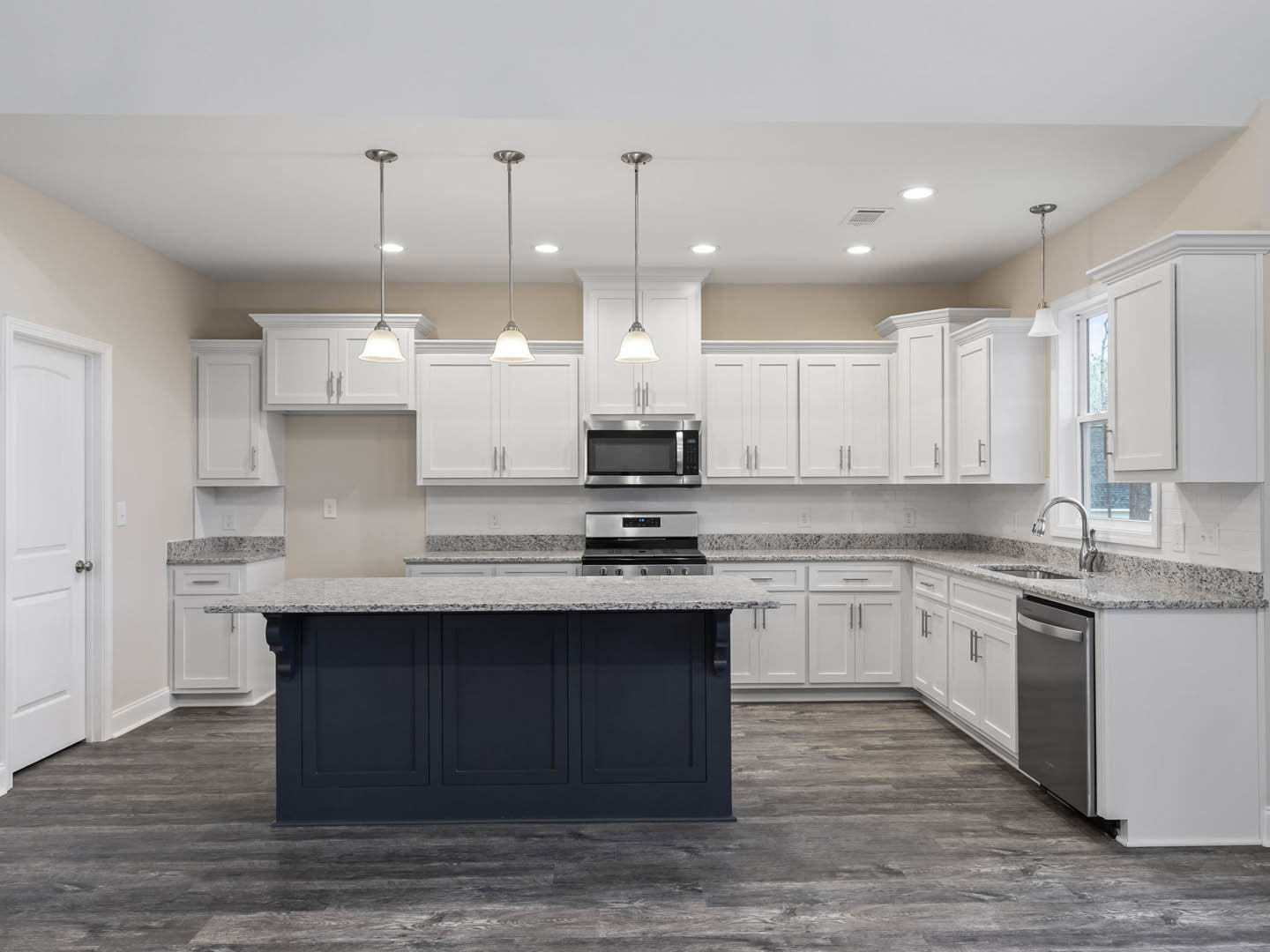 Kitchen with white shaker cabinets, granite countertops, stainless steel microwave and oven, central island, white door with silver hardware, and light tile flooring.