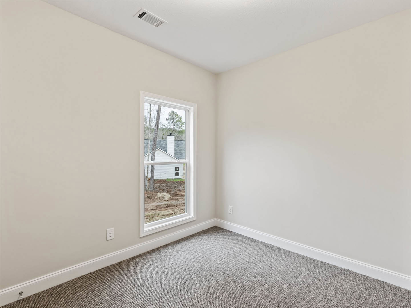 Bright room with white walls, large window overlooking trees, beige carpet flooring, ceiling vent, and decorative molding.