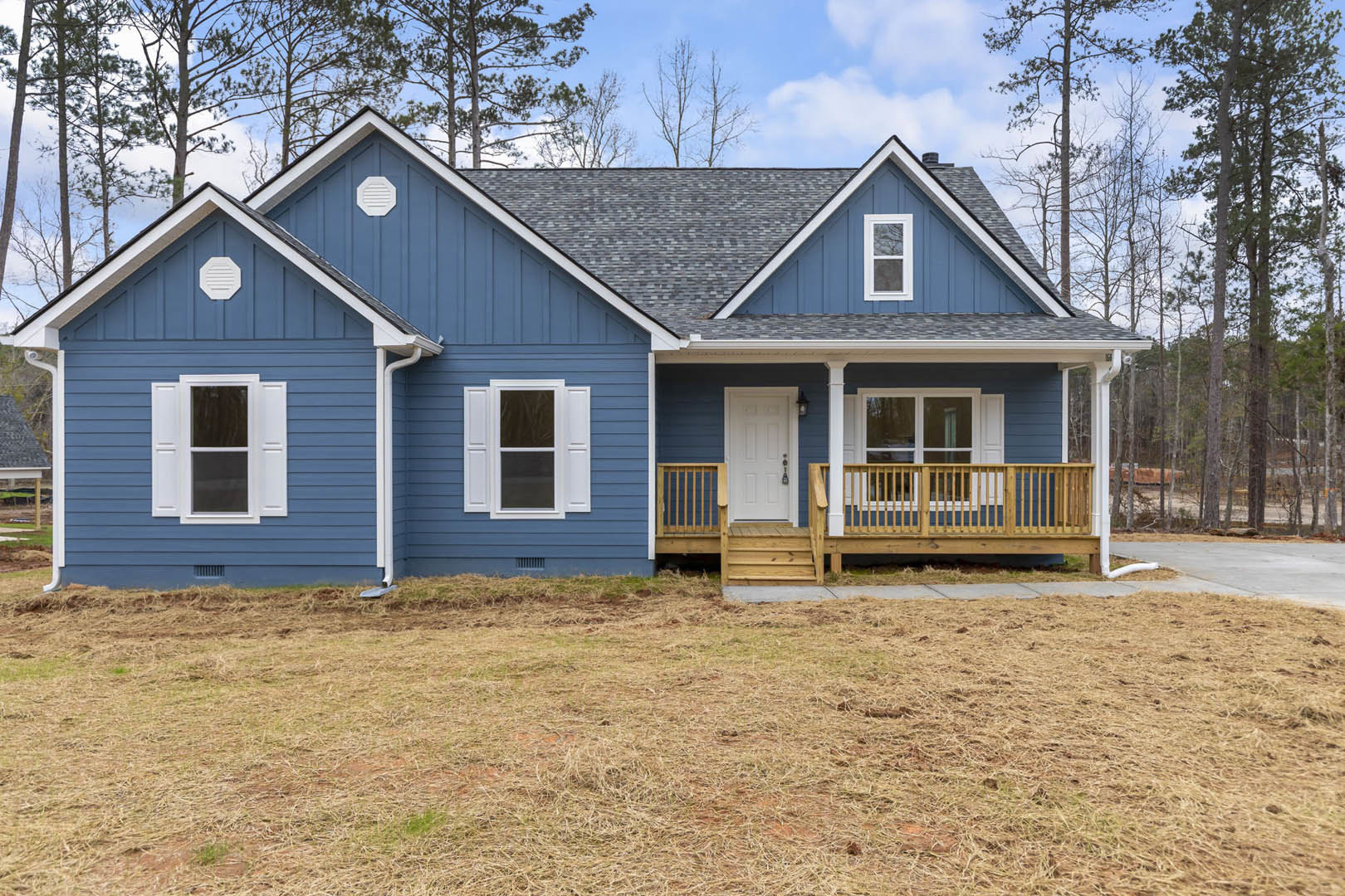 Blue house with white door and window frames, wooden porch railing, wood deck, and grassy yard.