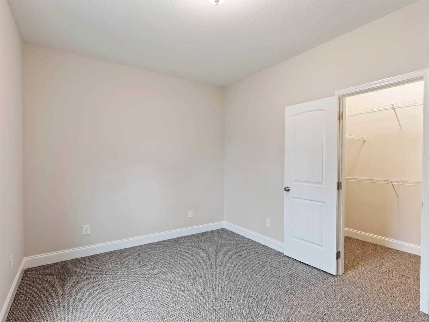 Bedroom with beige carpet, open white door featuring silver knob and square panels, built-in closet with shelving, white ceiling illuminated by recessed light