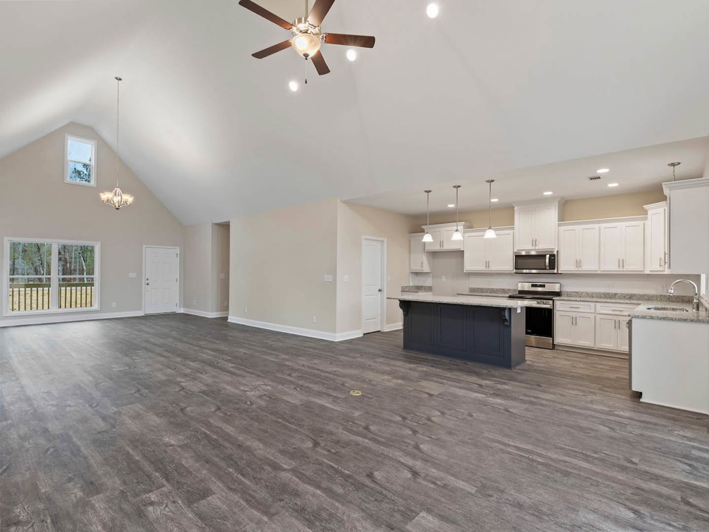 Spacious open floor plan featuring wood laminate flooring, central kitchen island with cabinetry, ceiling fan and light fixture, stainless steel stove and microwave, large window