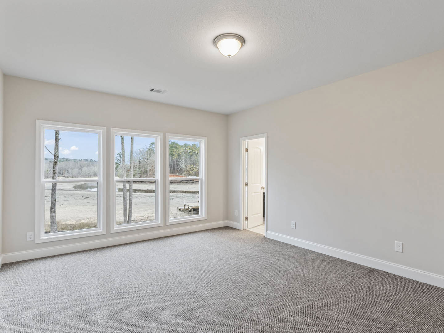 Carpeted room with white walls, open white door featuring glass handle, large windows overlooking river and trees, ceiling with recessed lighting and decorative molding